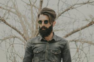 Ein bärtiger Mann mit Sonnenbrille steht vor einem Baum