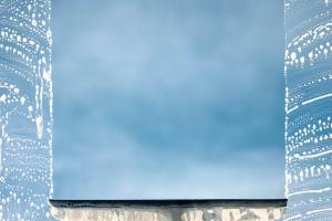 Ein schaumig eingeseiftes Fenster wird mit einem Abzieher gereinigt