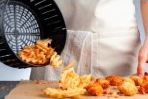 Person leert Garkorb einer Heißluftfritteuse auf Tisch